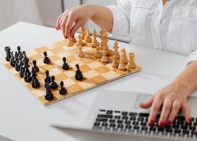 Close-up of a person playing chess and using a laptop indoors.