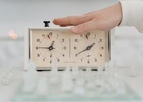 Close-up of a hand adjusting a chess clock during a timed chess game indoors.